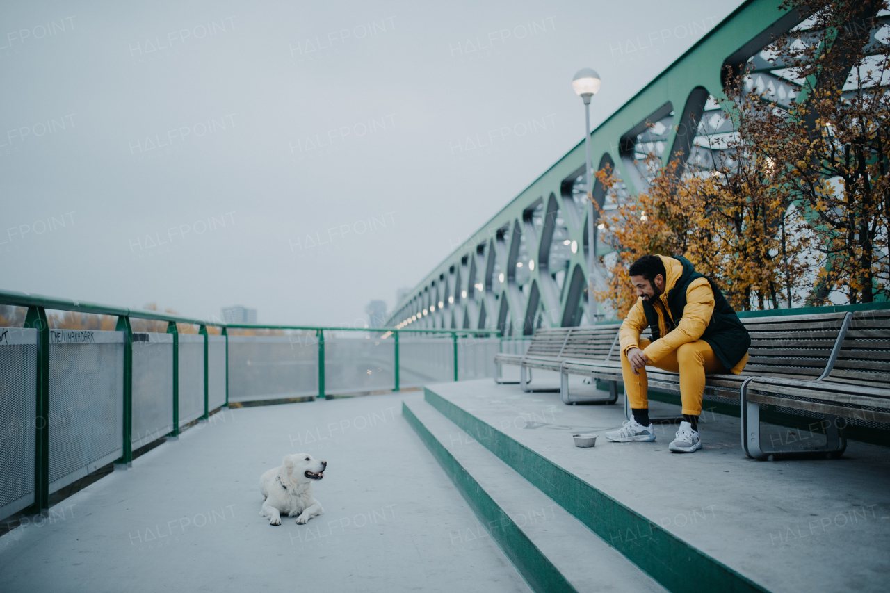 Happy young man resting in urban city area during dog walk outdoors in cloudy autumn day.