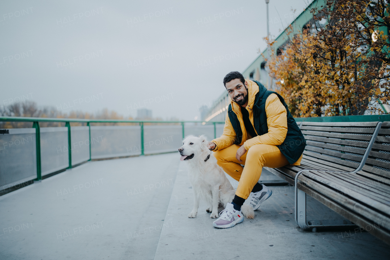 Happy young man resting in urban city area during dog walk outdoors in cloudy autumn day.