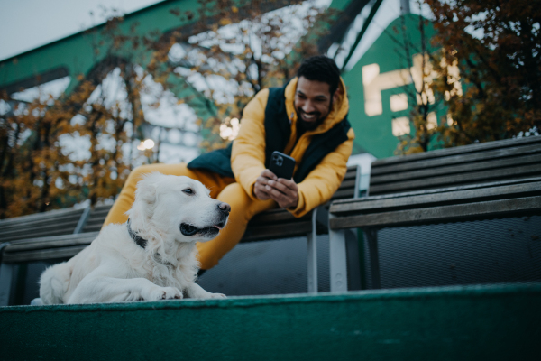 Happy young man resting and taking a foto of his dog in urban city area in autumn day.