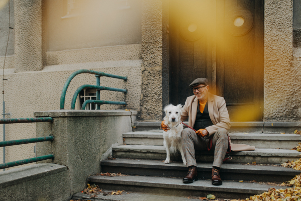 A happy senior man sitting on stairs and resting during dog walk outdoors in city.