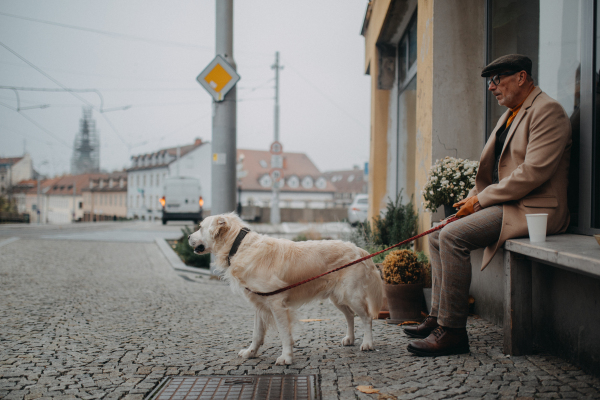 Unhappy senior man sitting on a bench in front of store and waiting somebody wih his big white dog