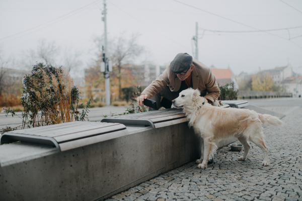 Elegant senior man with smartphone taking selfie with his big dog and walking outdoors in winter city.