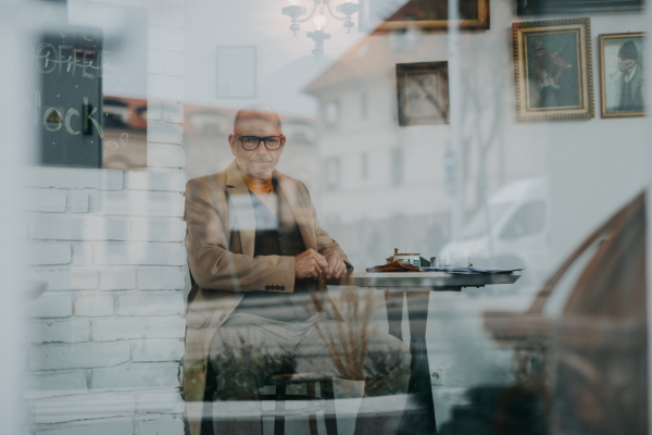 Elegant senior man sitting in a cafe and looking out of window.