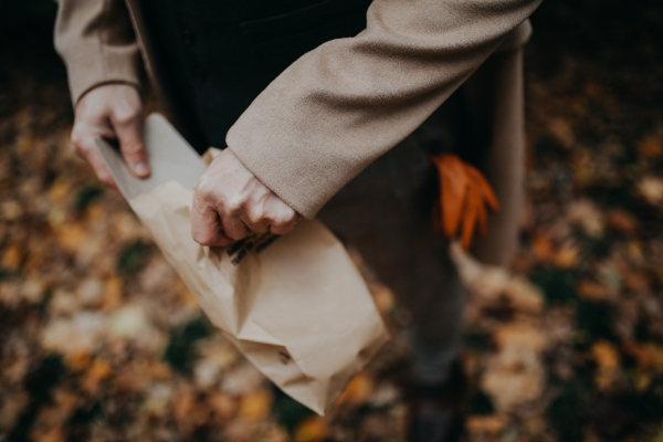 Close-up of a dog owner holding paper bag for excrements during walking in autumn citypark.