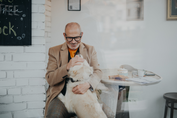 A happy senior man sitting in cafeteria and playing with his dog, shot through glass.