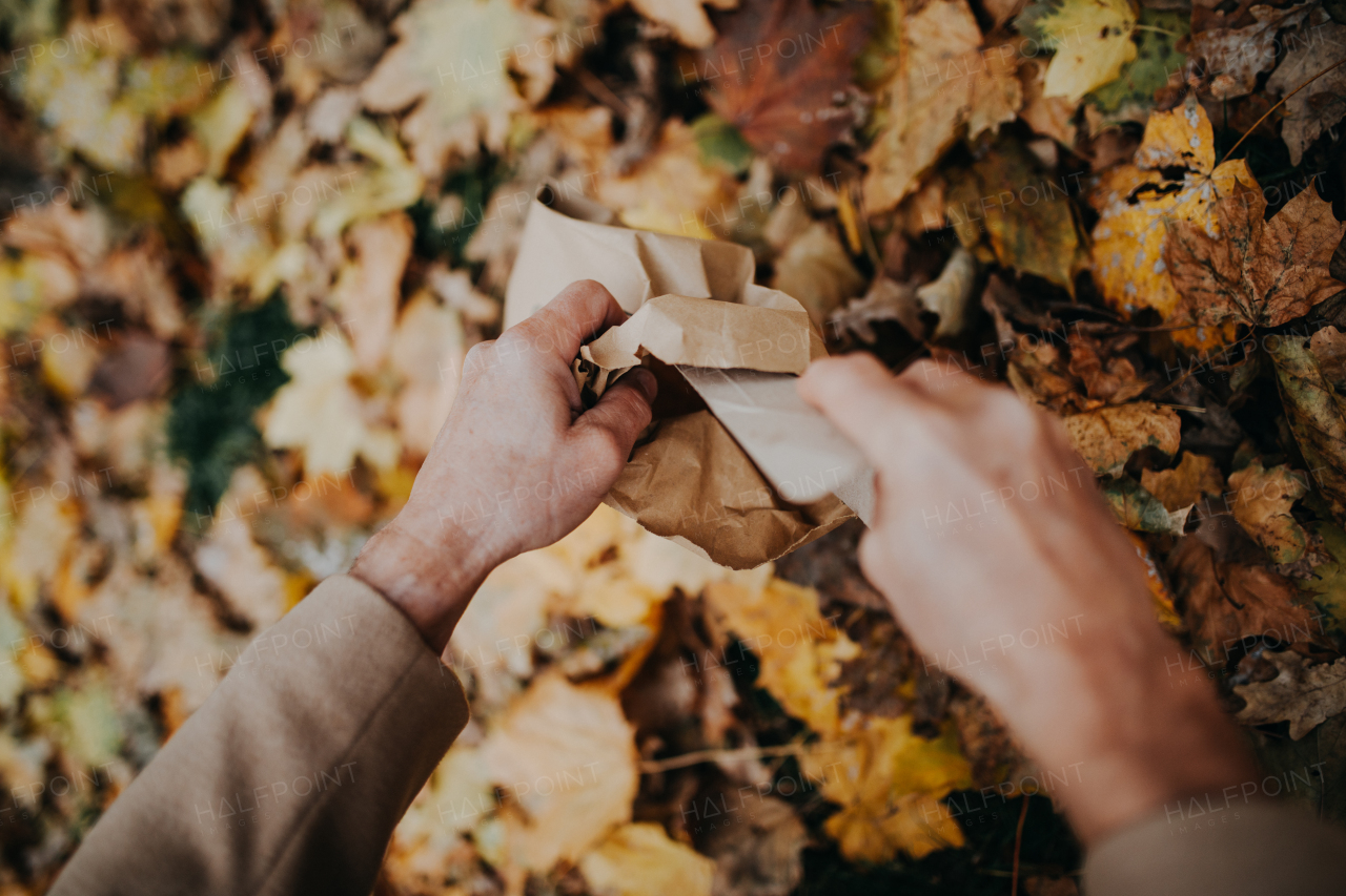 Close-up of dog owner picking excrements in the paper bag during walking in autumn citypark.