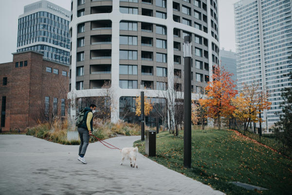 A rear view of young man with ffp2 mask running with his dog on leash outdoors in city park.