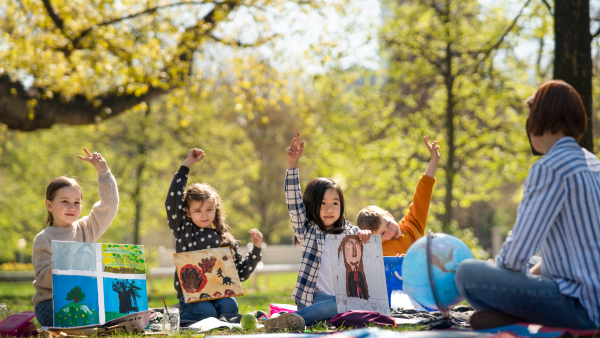 A teacher with small children sitting outdoors in city park, learning group education and art concept.