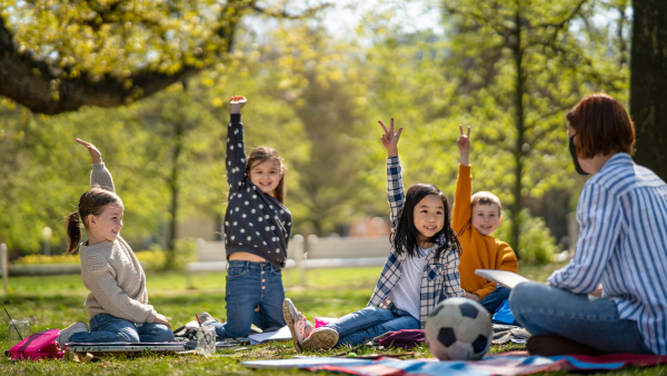 A teacher with small children sitting outdoors in city park, learning group education and art concept.