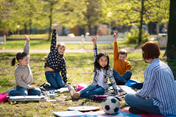 A teacher with small children sitting outdoors in city park, learning group education concept.