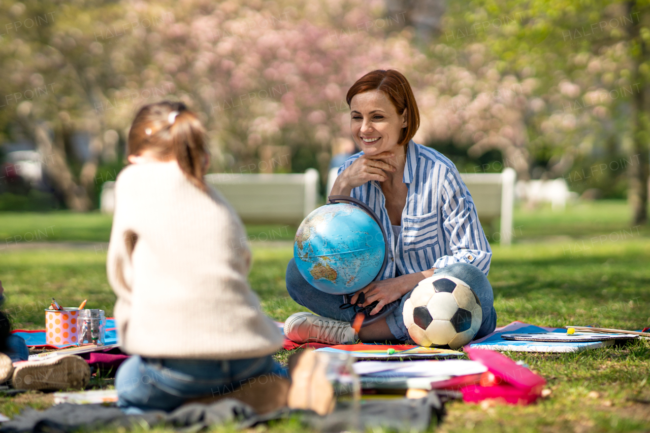 A teacher with small children sitting outdoors in city park, learning group education concept.