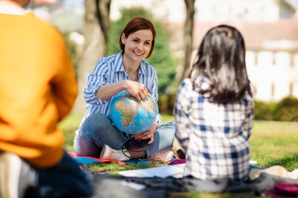 A teacher with small children sitting outdoors in city park, learning group education concept.