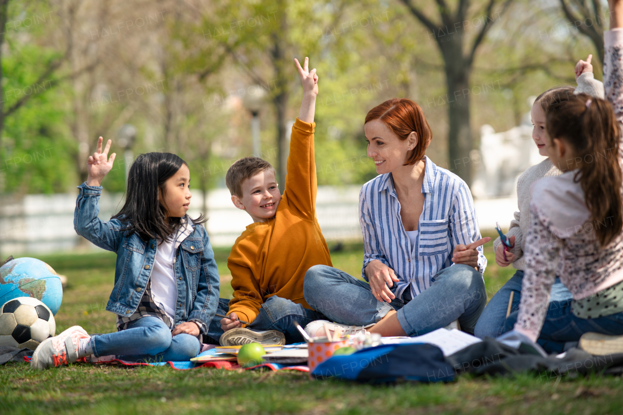 A teacher with small children sitting outdoors in city park, learning group education concept.