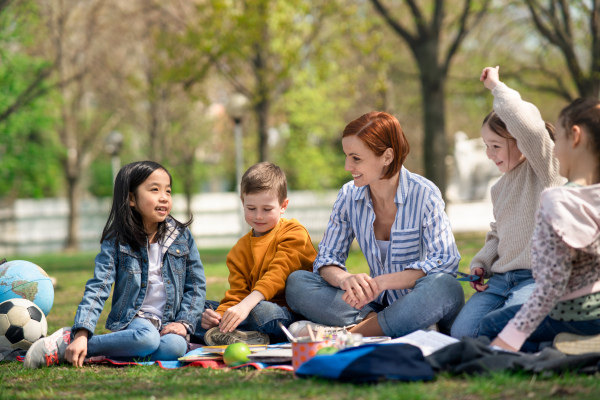 A teacher with small children sitting outdoors in city park, learning group education concept.