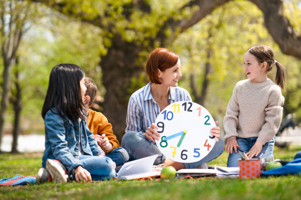 A teacher with small children sitting outdoors in city park, learning group education concept.