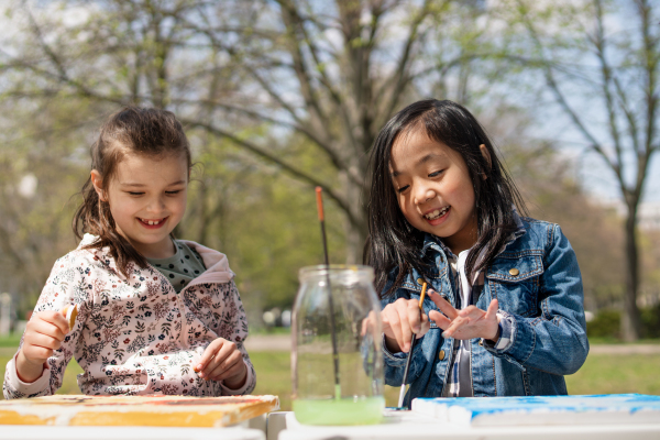 Portrait of small children painting pictures outdoors in city park, learning group education concept.