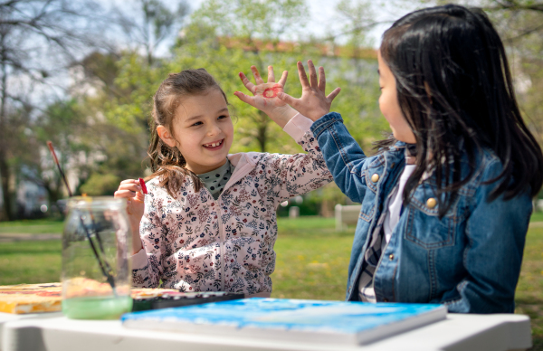 Portrait of small children painting pictures outdoors in city park, learning group education concept.