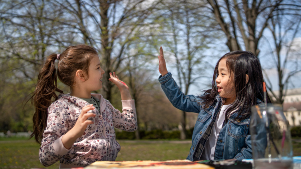 Portrait of small children painting pictures outdoors in city park, learning group education concept.