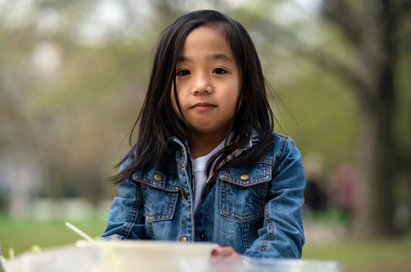 Portrait of small child looking at camera outdoors in city park, learning group education concept.