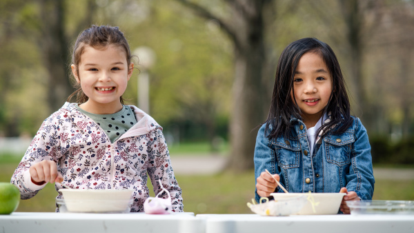 Happy small children eating lunch outdoors in city park, learning group education concept.