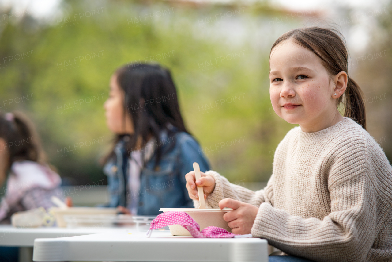 Happy small children eating lunch outdoors in city park, learning group education concept.