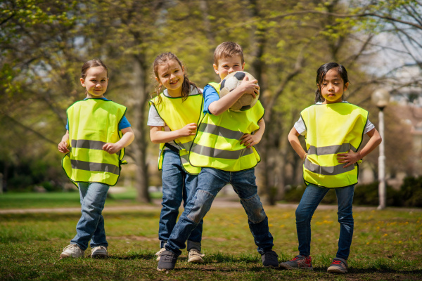 A small children with ball looking at camera outdoors in city park, learning group education concept.