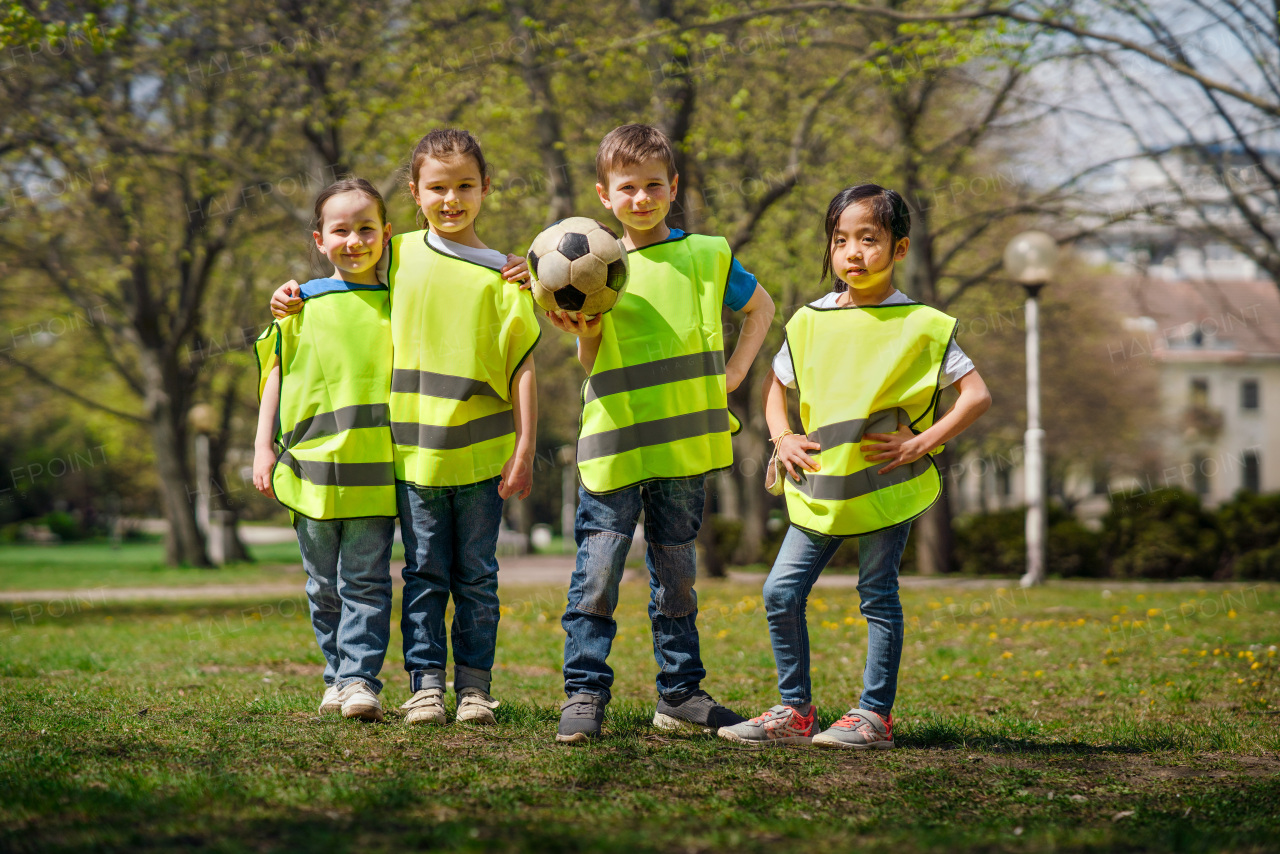 A small children with ball looking at camera outdoors in city park, learning group education concept.