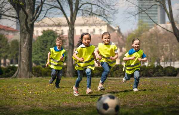 Happy small children playing football outdoors in city park, learning group education concept.