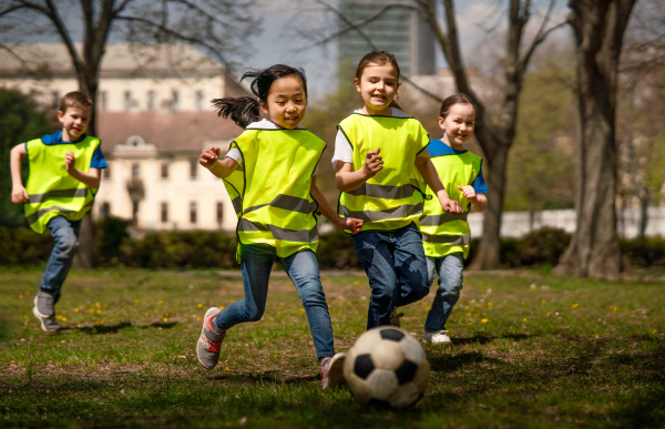 Happy small children playing football outdoors in city park, learning group education concept.