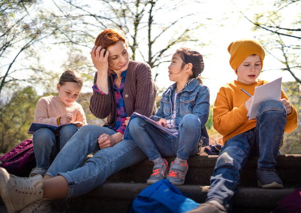 A teacher with small children sitting outdoors in city park, learning group education concept.