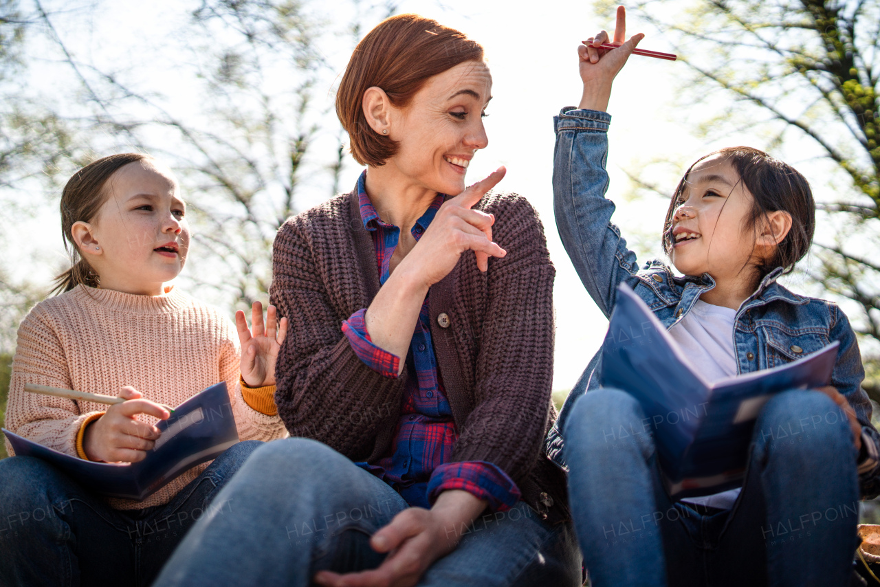 A teacher with small children sitting outdoors in city park, learning group education concept.