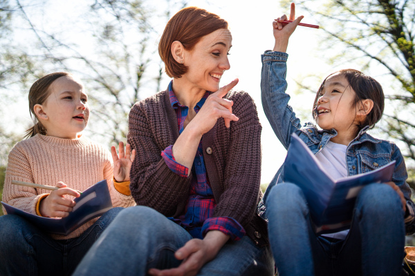 A teacher with small children sitting outdoors in city park, learning group education concept.