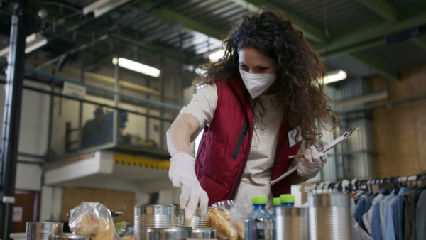 Woman volunteer in community donation center, food bank and coronavirus concept.