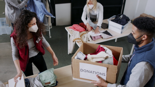 Top view of woman volunteer working with clothes in community charity donations center, looking at camera. Coronavirus concept.