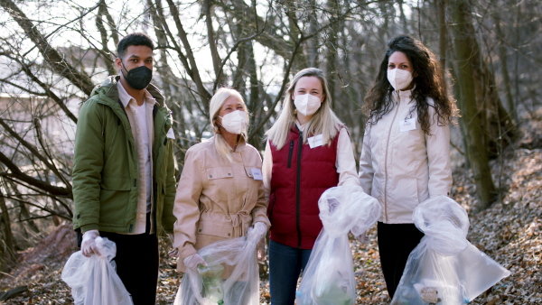 A group of volunteers picking up plastic waste from nature, looking at camera. Coronavirus concept.