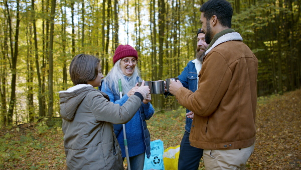 A diverse group of happy volunteers cleaning up forest, having break, drinking tea and talking together.