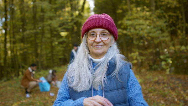 A senior woman volunteer looking at camera when cleaning up forest from waste, community service concept.