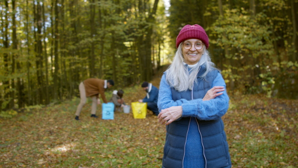 A senior woman volunteer looking at camera when cleaning up forest from waste, community service concept.