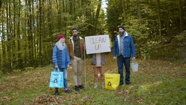 A diverse group of irritated activists ready to clean up forest, holding banner and looking at camera.