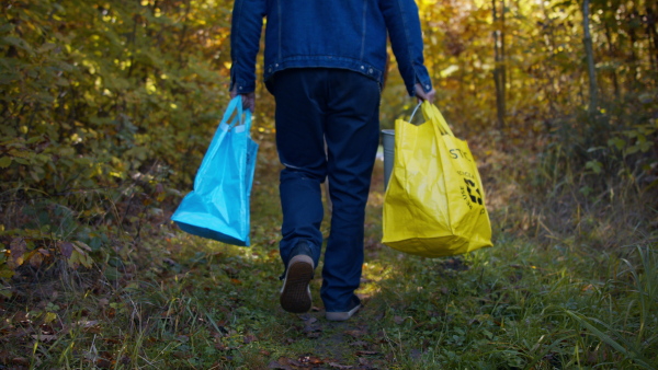 A rear view of volunteers carrying recycling bags after cleaning up forest from waste, community service concept