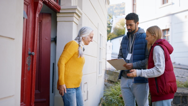 Young door to door volunteers talking to senior woman and taking a survey at her front door.