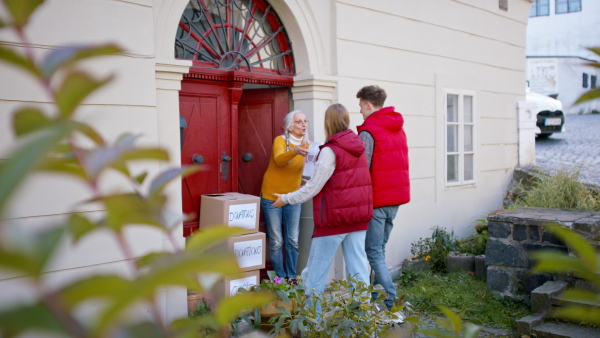 A diverse group of volunteers taking donation boxes from senior woman outdoors, social care and charity concept