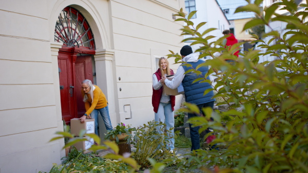 A diverse group of volunteers taking donation boxes from senior woman outdoors, social care and charity concept