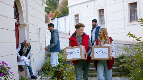 A diverse group of volunteers taking donation boxes from senior woman outdoors, social care and charity concept