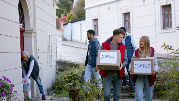 A diverse group of volunteers taking donation boxes from senior woman outdoors, social care and charity concept