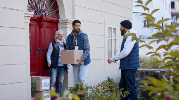 A diverse group of volunteers taking donation boxes from senior woman outdoors, social care and charity concept