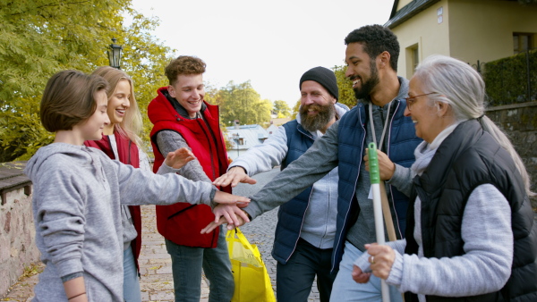 A diverse group of happy community service volunteers stacking hands together outdoors in street