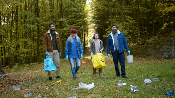 A diverse group of volunteers cleaning up forest from waste, standing and looking at camera, community service concept