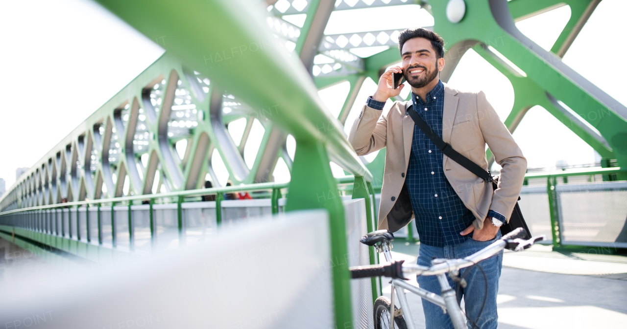 Portrait of young business man commuter with bicycle going to work outdoors in city, using smartphone.