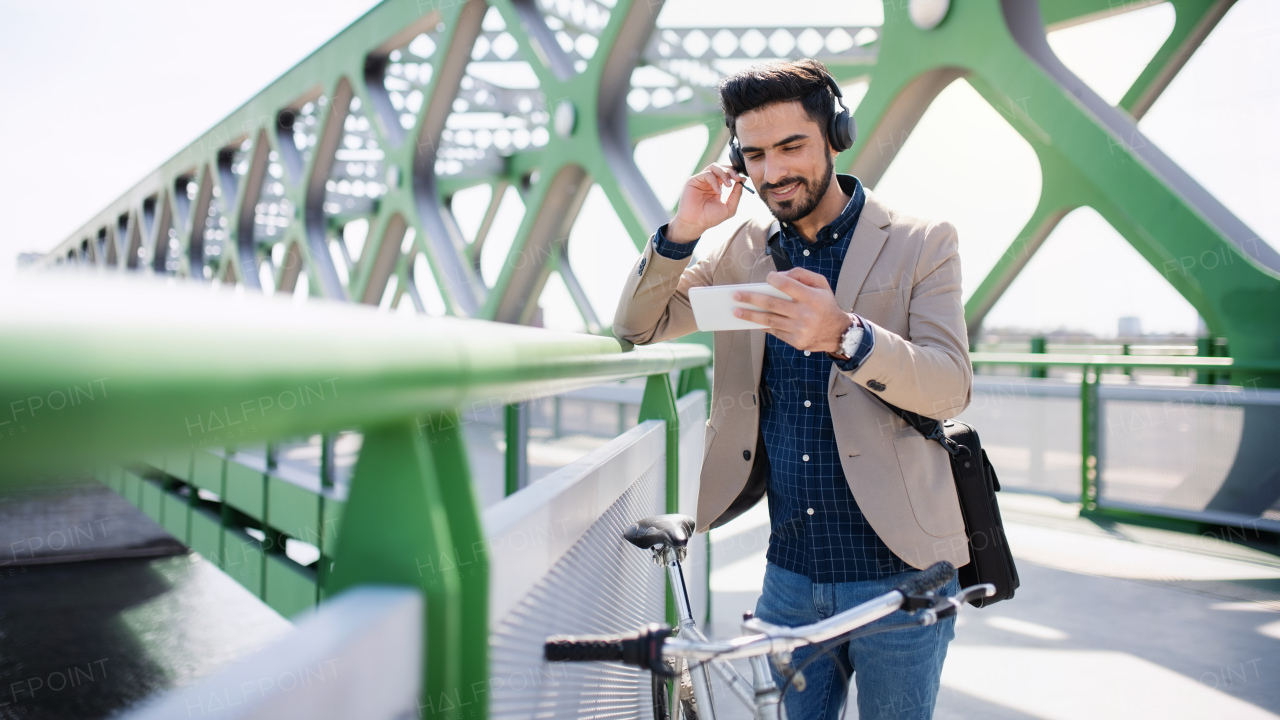 A young business man commuter with bicycle going to work outdoors in city, video call on smartphone.